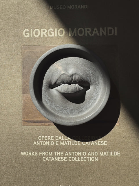 Ash Grey Lip Incense Burner styled on Giorgio Morandi art book with dramatic shadow.