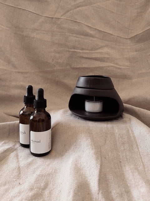 Nomad Room Oil bottles styled with black ceramic oil burner on neutral linen background.