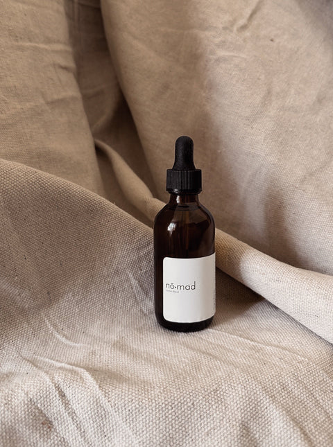 Nomad Room Oil amber glass bottle on neutral linen background.
