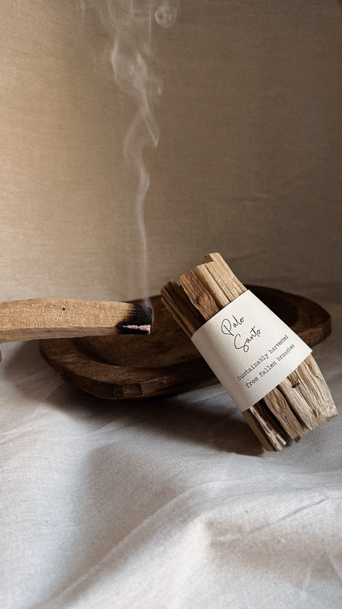 Palo Santo bundle with smoke styled on wooden bowl and neutral linen background.