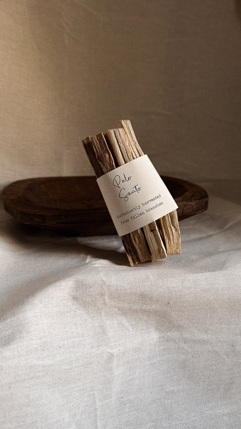 Palo Santo bundle with smoke styled on wooden bowl and neutral linen background.