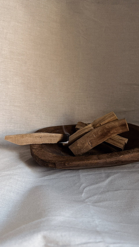Burning Palo Santo stick resting over wooden bowl with soft smoke.