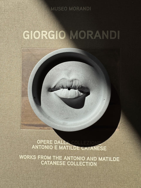 Ash Grey Lip Incense Burner styled on Giorgio Morandi art book with dramatic shadow.