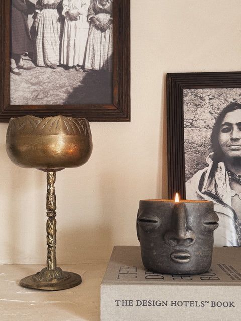 Oaxaca face candle in bronze glass vessel styled with book and framed photograph in warm interior setting.