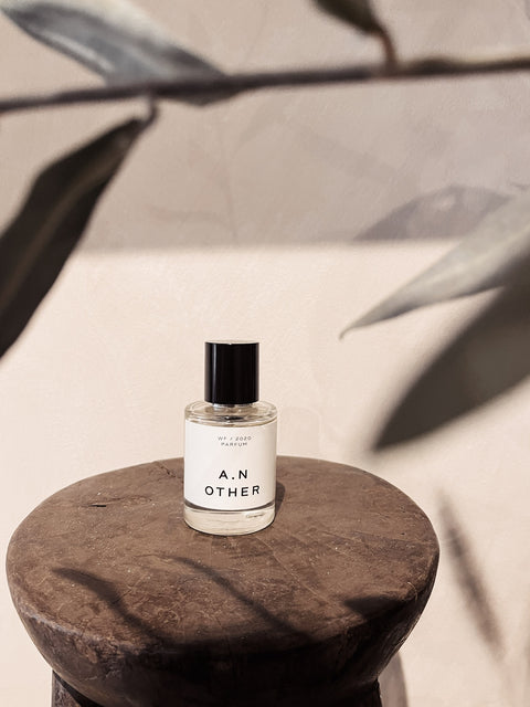 A.N. Other Ultimate Patchouli WF/2020 Parfum 50ML bottle on rustic wood pedestal with warm beige wall and botanical shadow.